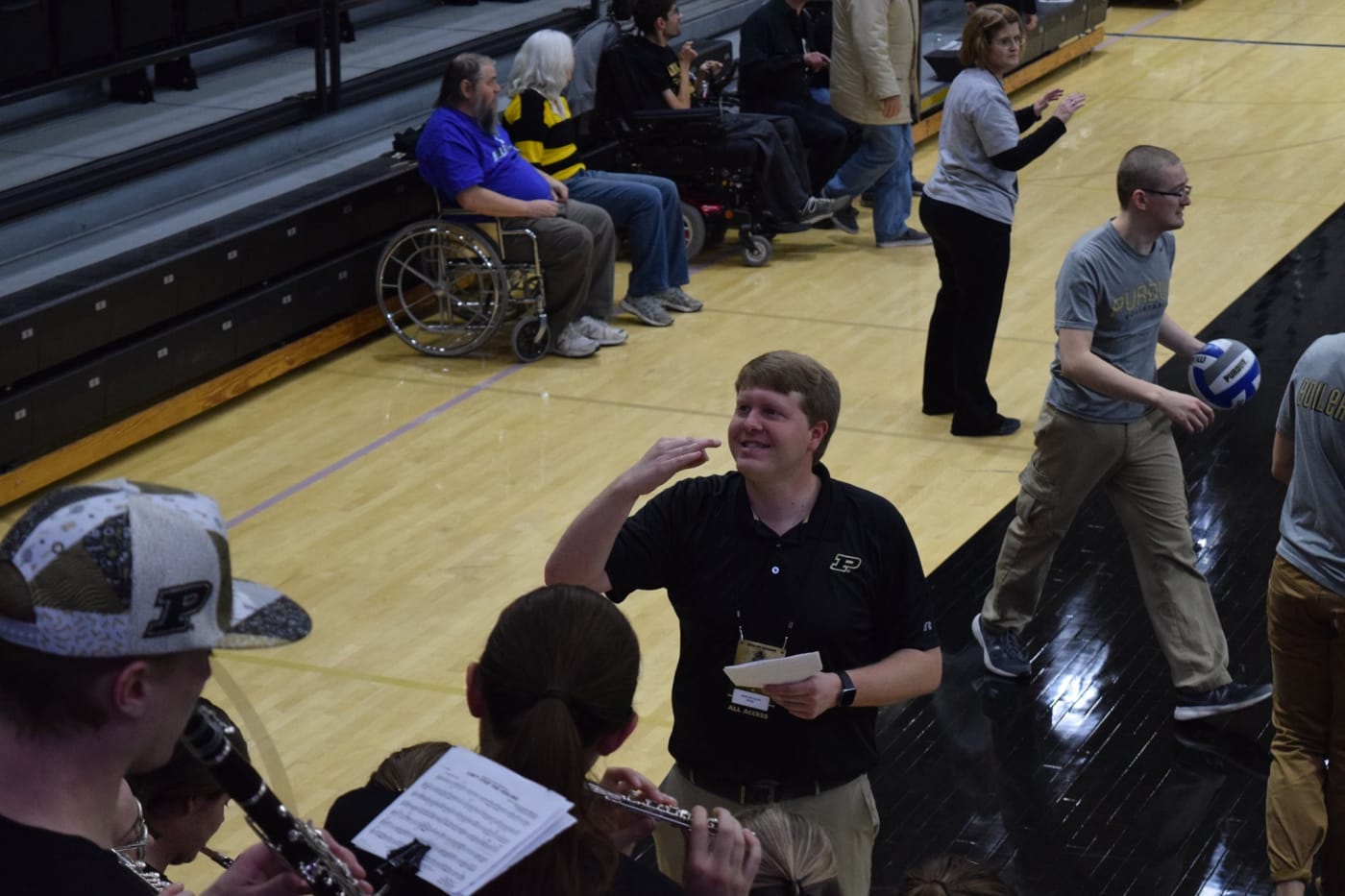 A man conducts with his right hand to a group of players on bleachers