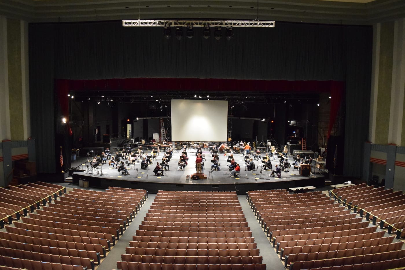 A large stage at a theater, players sitting social-distanced apart from each other.